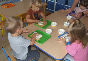 Dzieci smarują herbatniki białym serkiem.