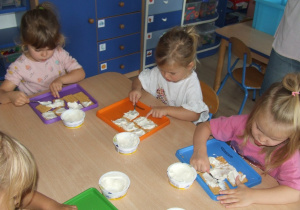 Dzieci smarują herbatniki białym serkiem.