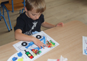 Chłopiec wypełnia farbą kółka za pomocą palców.