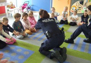 Pani policjantka pokazuje dzieciom pozycję bezpieczną.