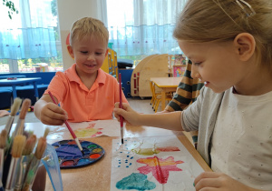 Dzieci malują pędzlaem po kartce jesienne krajobrazy.