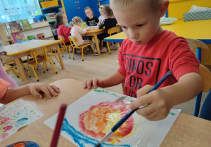 Chłopiec maluje kolorowy, jesienny liść farbami akwarelowymi.