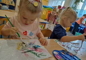 Dziewczynki malują farbami po kartce kompozycje jesienne.