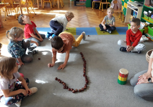 Dzieci układają węża z kasztanów.