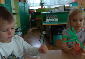 Dzieci siedzą przy stoliku i napełniają woreczek foliowy pomarańczową bibułą.