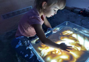 Dziewczynka rysuje i bawi się kaszą manną na panelu swietlnym.