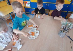 Dzieci przy stoliku malują farbami szablon wiewiórki.