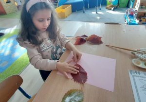 Dziewczynka przykleja liść do kartki.
