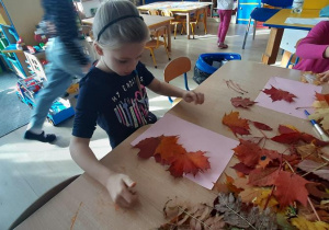 Dziewczynka przykleja liście do kartki, robiąc ogon wiwiórki.