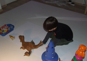 Chłopiec odrysowuje kształt cienia dinozaura.