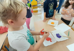 Chłopiec maluje farbą swoją dłoń.