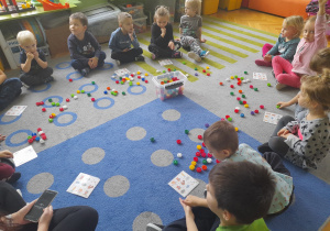 Dzieci siedzą na dywanie i grają w bingo.