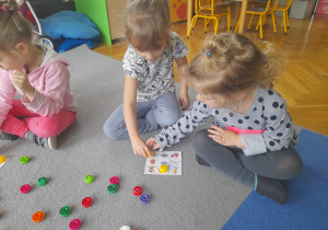 Dziewczynki siedzą na dywanie i grają w bingo.