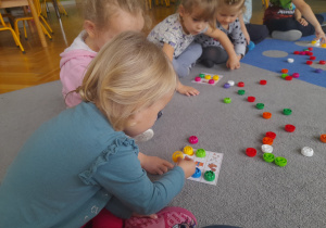 Dziewczynki siedzą na dywanie i grają w bingo.