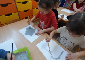 Dzieci malują szara farbą białą kartkę.