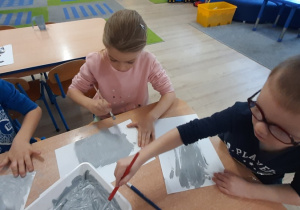 Dzieci malują szara farbą białą kartkę.