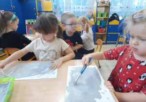 Dziewczynki malują szara farbą białą kartkę.