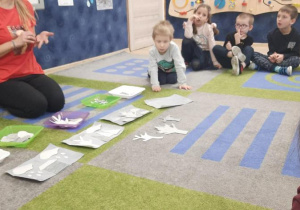 Nauczycielka pokazuje na dywanie szare obrazki, które będą układać na swojej kartce.