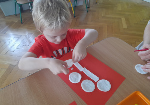 Chłopiec przykleja elementy na papier.