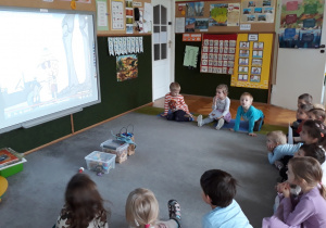 Dzieci oglądają film o dinozaurach na tablicy multimedialnej.