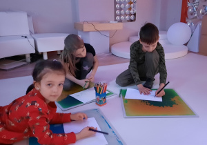 Dzieci rysują na kartonach rozłożonych na podłodze.