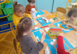 Dzieci przyklejają elementy na papier tworząc karmnik.