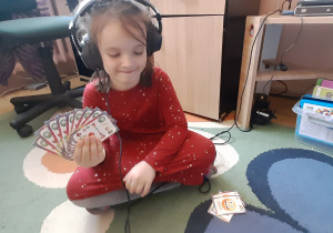 Dziewczynka ze słuchawkami na uszach, trzyma w dłoni karty "Piotruś" i gra z nauczycielką.