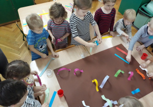 Dzieci wykonują wspólną pracę plastyczną z pasków papieru.