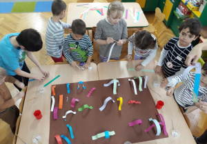 Dzieci wykonują wspólną pracę plastyczną z pasków papieru.
