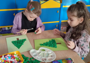 Dziewczynki przyklejają zielony makaron kokardka do kartki.