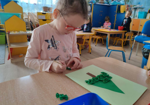 Dziewczynka przykleja zielony makaron kokardka do kartki.