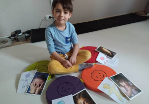 Chłopiec prezentuje emocje dzieci na obrazkach.