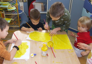 Dzieci malują karton żółtą farbą