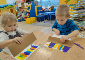 Dzieci rozprowadzają farbę na kartce.
