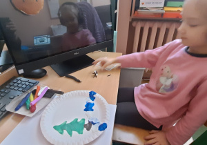 Dziewczynka na talerzu papierowym wykleja plasteliną zimowy obrazek.