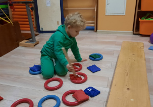 Chłopiec siedzi na podłodze i układa woreczki w kołach ringo.