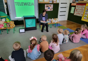Dzieci słuchają jak nauczycielka czyta książkę.