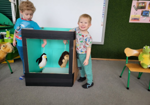 Dzieci animują maskotkami w telewizorze wykonanym z pudła kartonowego.