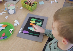 Chłopiec wykonuje ekran telewizyjny wykorzystując kolorowe papiery i wyklejanki