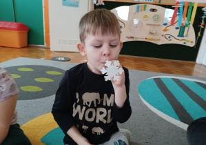 Chłopiec przy pomocy słomki podnosi papierową śnieżynkę