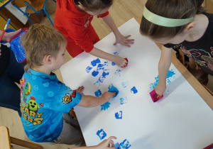 Dzieci tapują foremkami białe tło niebieską farbą.