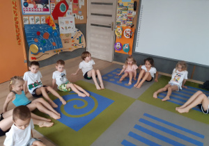 Dzieci siedzą na dywanie i ćwiczą.