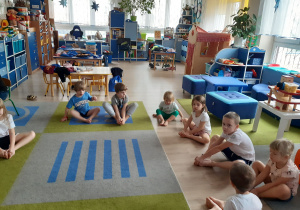 Dzieci siedzą na dywanie i ćwiczą.
