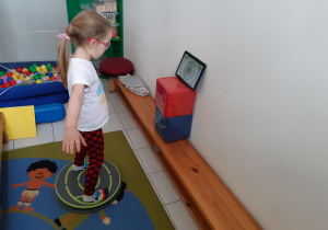Dziewczynka stoi na platformie balansowej i steruje grą na tablecie.