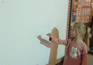 Dziewczynka wykonuje sekwencję gestów tworząc cienie na tablicy.