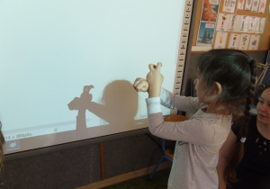 Dziewczynka wykonuje sekwencję gestów tworząc cienie na tablicy.