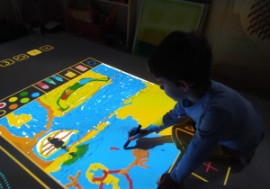 Chłopiec rysuje mapę na podłodze interaktywnej.