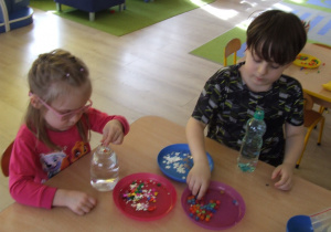 Dzieci dorzucają koraliki i błyszczące przedmioty do butelki z wodą i gliceryną.