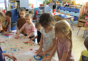 Dzieci rozsmarowują farbę całymi dłońmi w rytm muzyki.