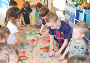 Dzieci rozsmarowują farbę całymi dłońmi w rytm muzyki.